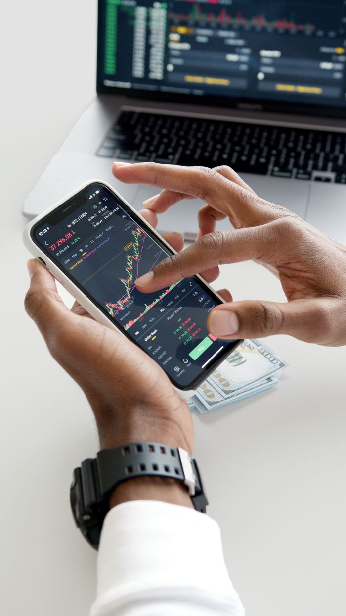 project-02-d Hands using smartphone trading app with charts, dollar bills in background.